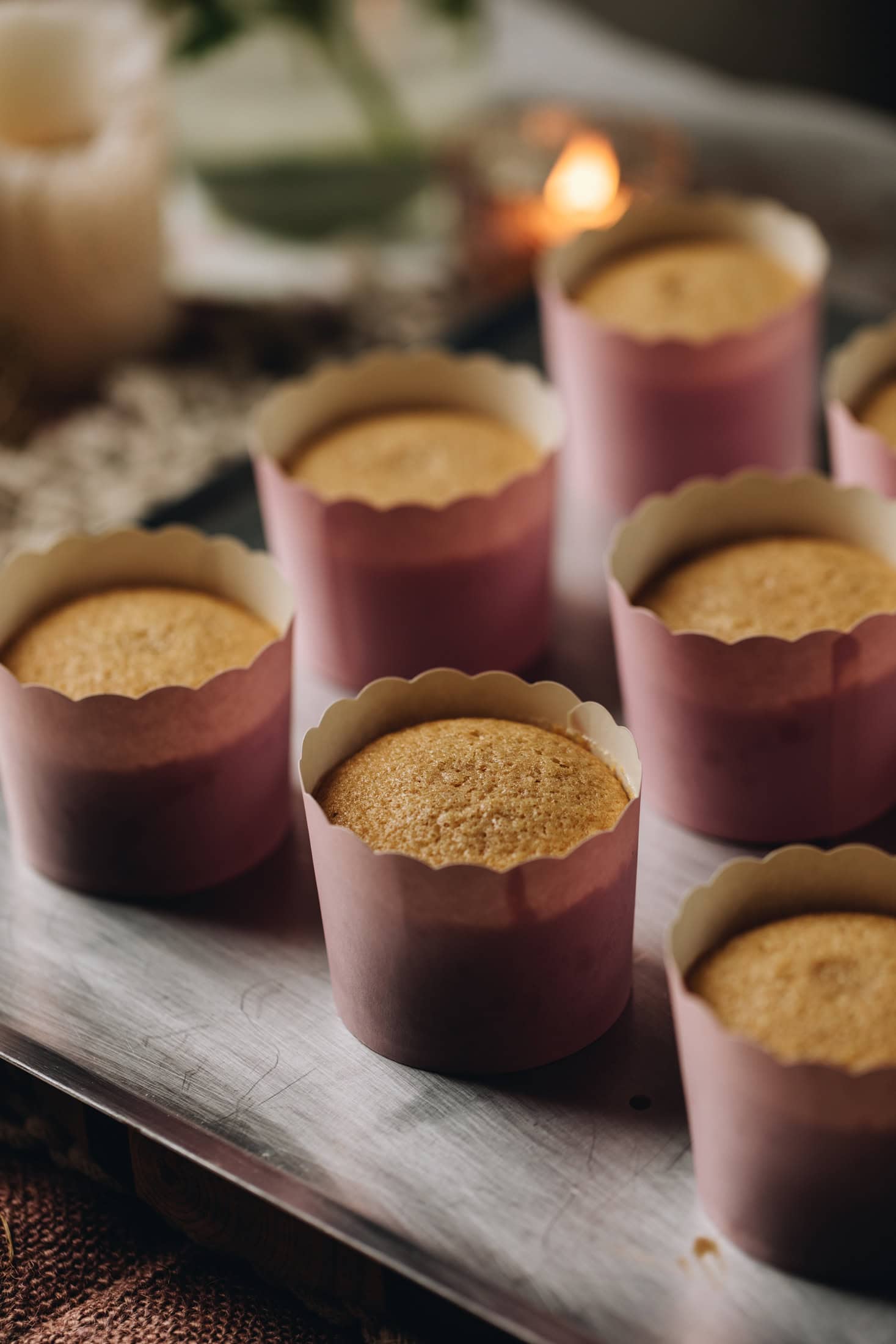 Freshly baked brown butter vanilla cupcakes in pink cardboard cases are on a silver tray.
