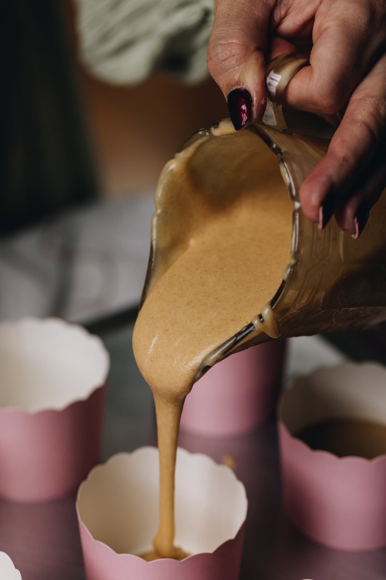The cupcake batter is in a vintage glass jug, it is being poured in to pink cardboard cupcake cases.