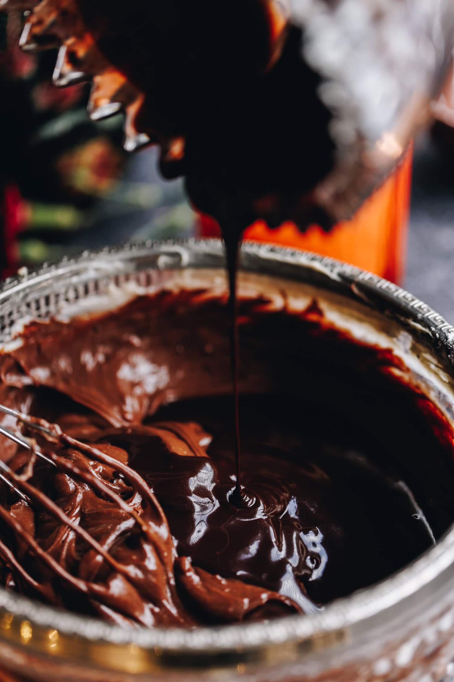 A glass bowl has a chocolate mixture in it, pour in to the bowl is melted chocolate. 