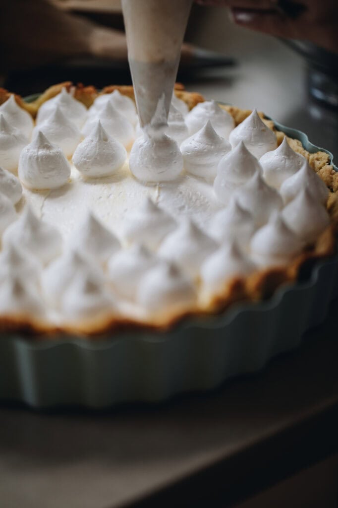 A close up of a piping bag piping meringue on to the Homemade Lemon Meringue Pie.