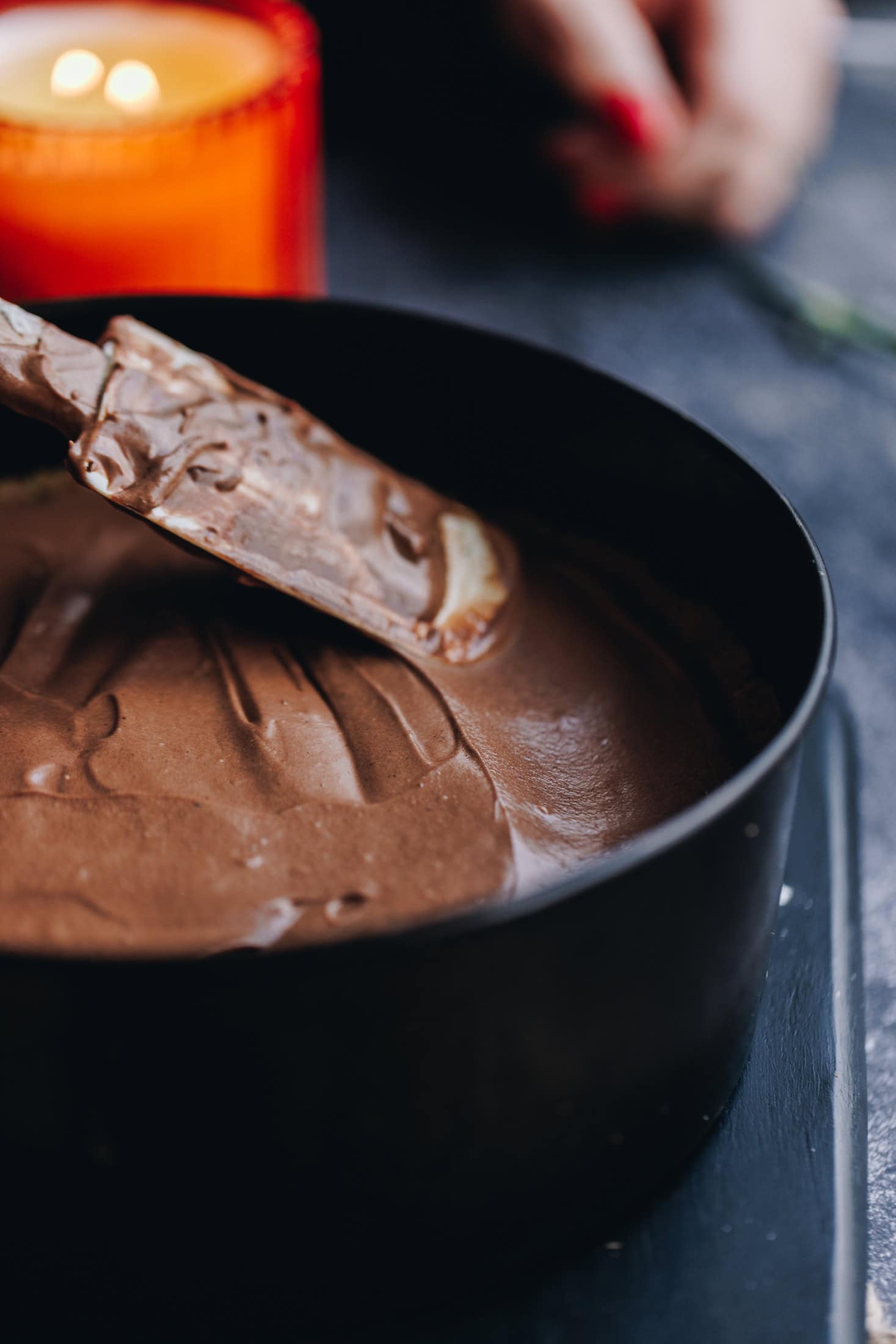 Into a cake tin a chocolate cheesecake filling is being spread out with a spatula. 