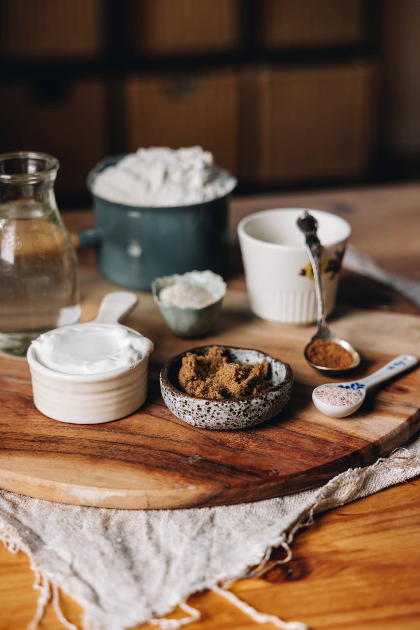 Dough ingredients are placed on a wooden board, each ingredient is placed in a vintage bowl, jar or spoon. 