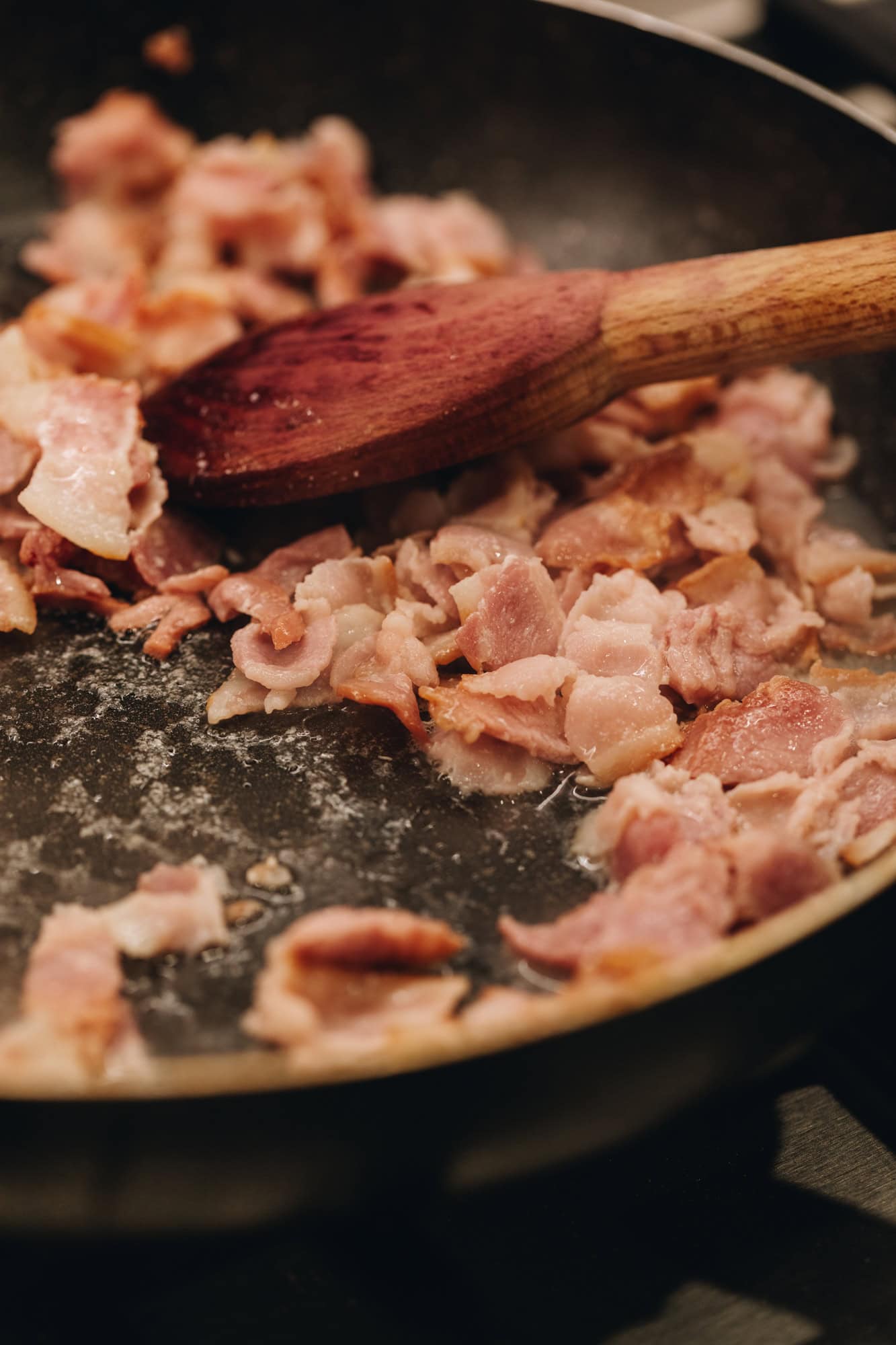 Chopped pieces of bacon are frying in a pan