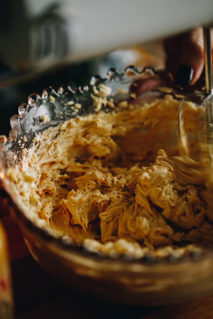 Close up of the peanut butter buttercream being whipped with a white hand mixer. It is an action shot of the butter being whipped.