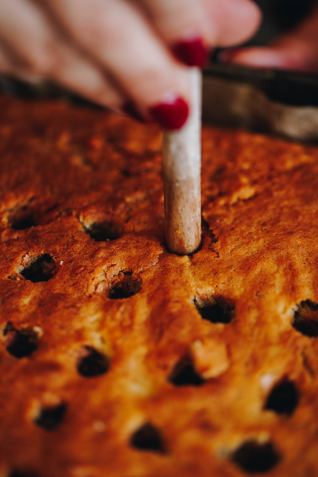 A close up shot of the freshly banana cake shows holes have been poked in to it. A wooden handle is poking a hole in it. 
