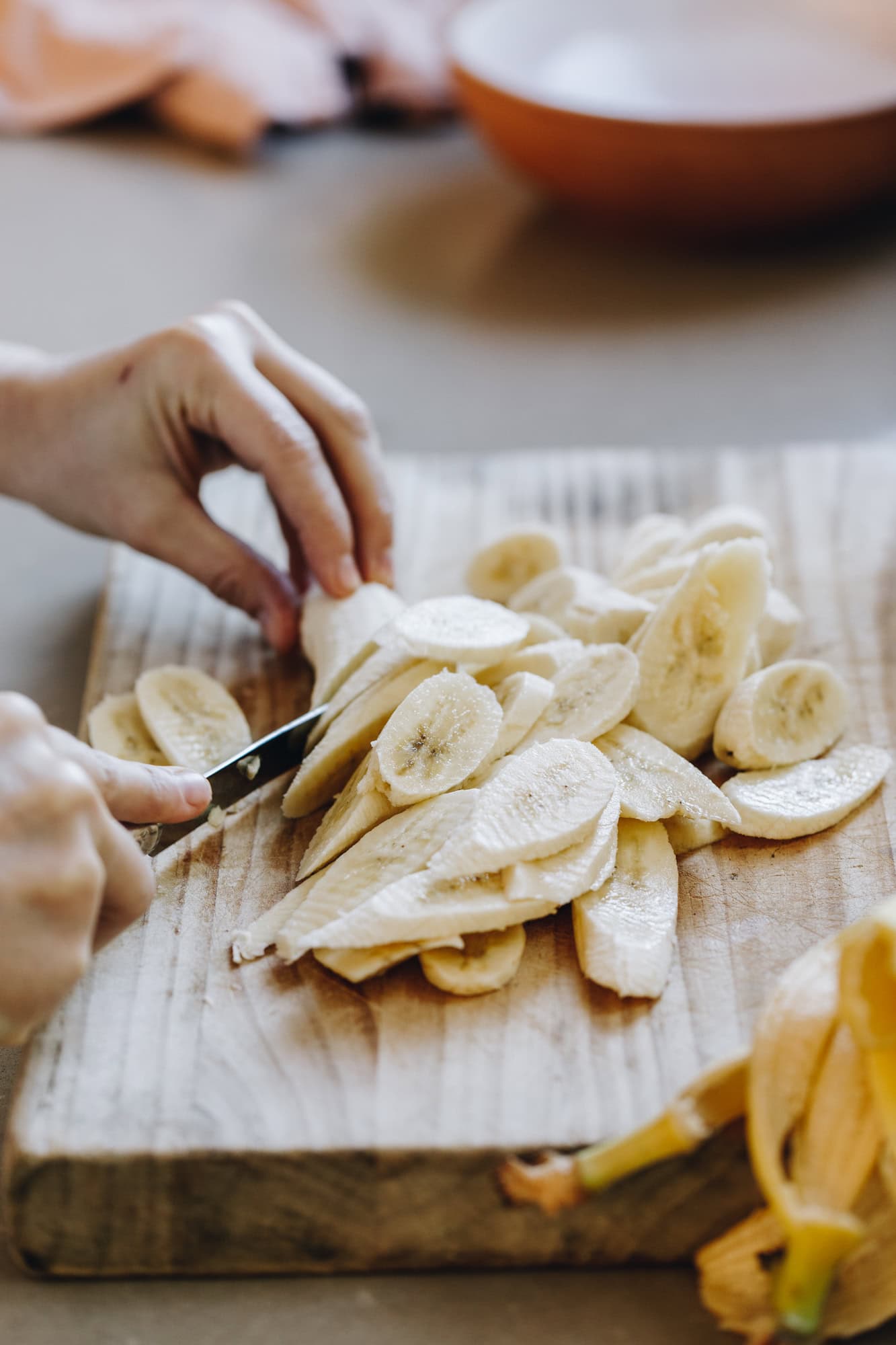 A wooden board has bananas on it that are being sliced in to long pieces. The board is on a grey stone bench. 