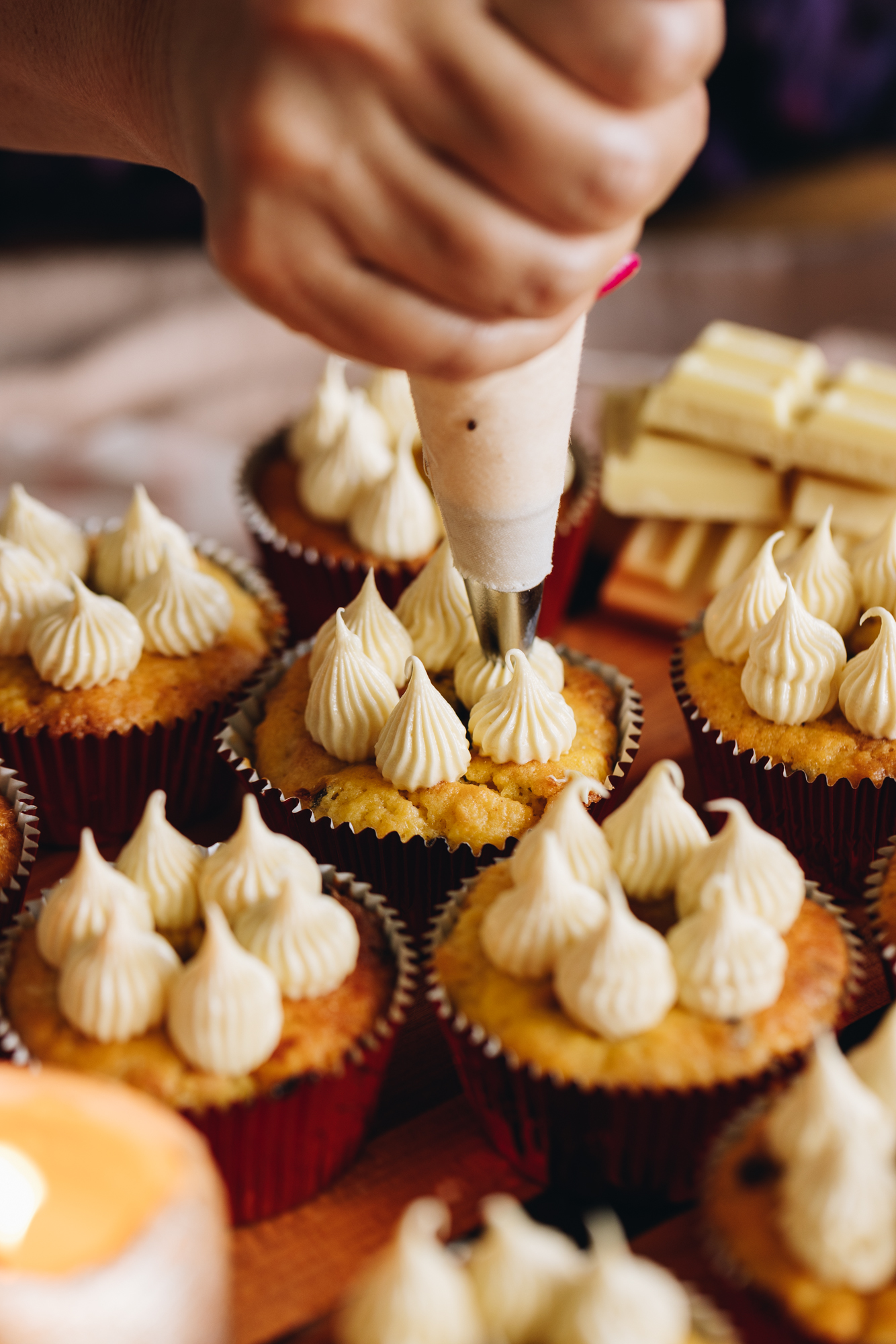 Passionfruit White Chocolate Muffins are being decorated with a simple buttercream. They are being piped on. 