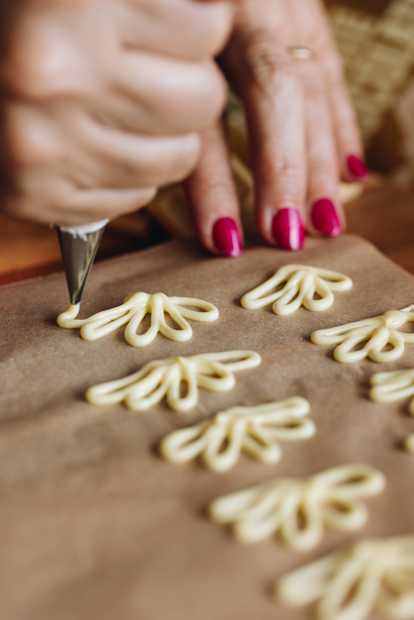 White chocolate fan decorations are piped on to borrow baking paper. Naomi is piping the last decoration. 