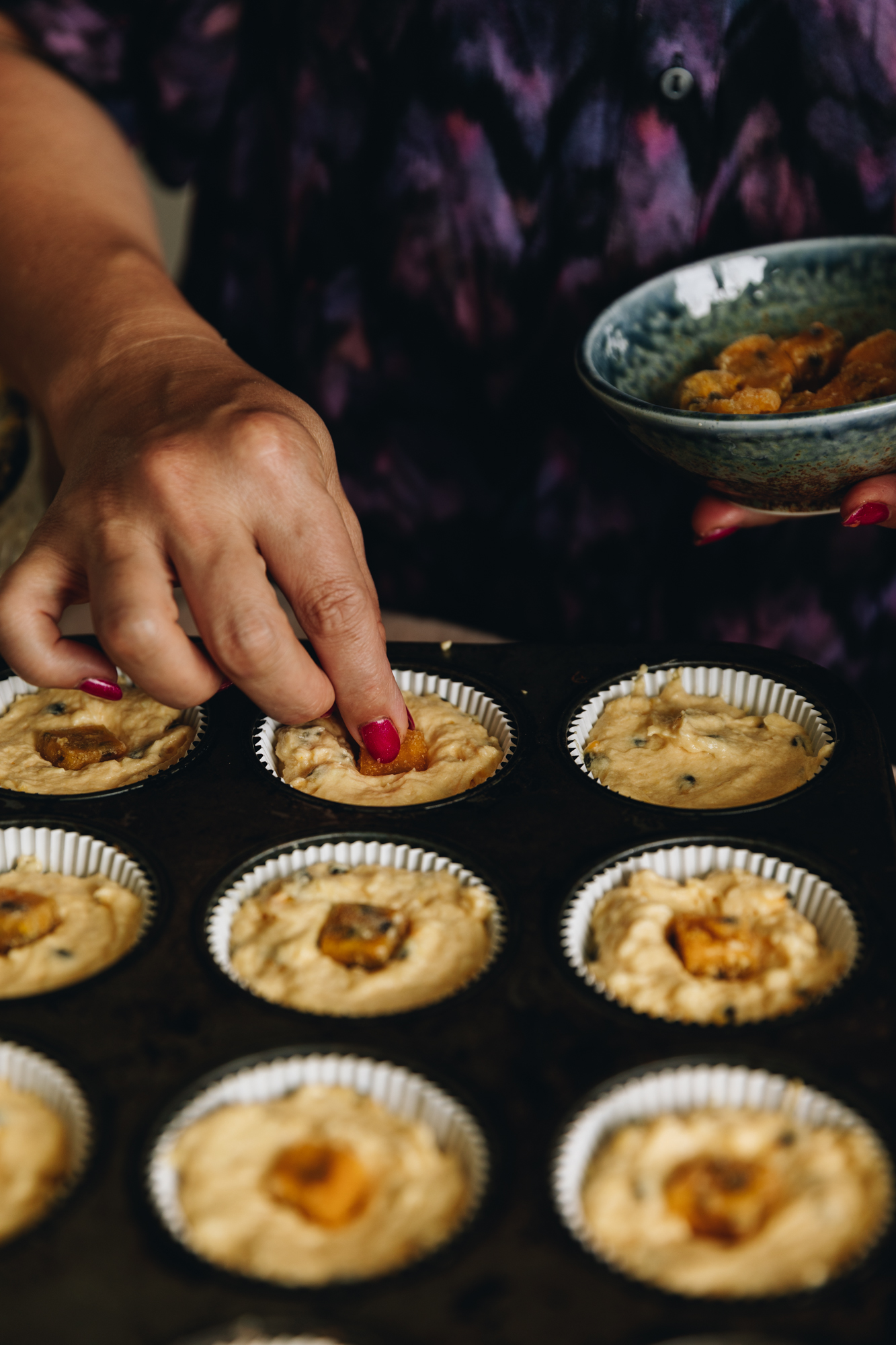 A tray of muffins are having passionfruit squares placed in the centre before baking. 
