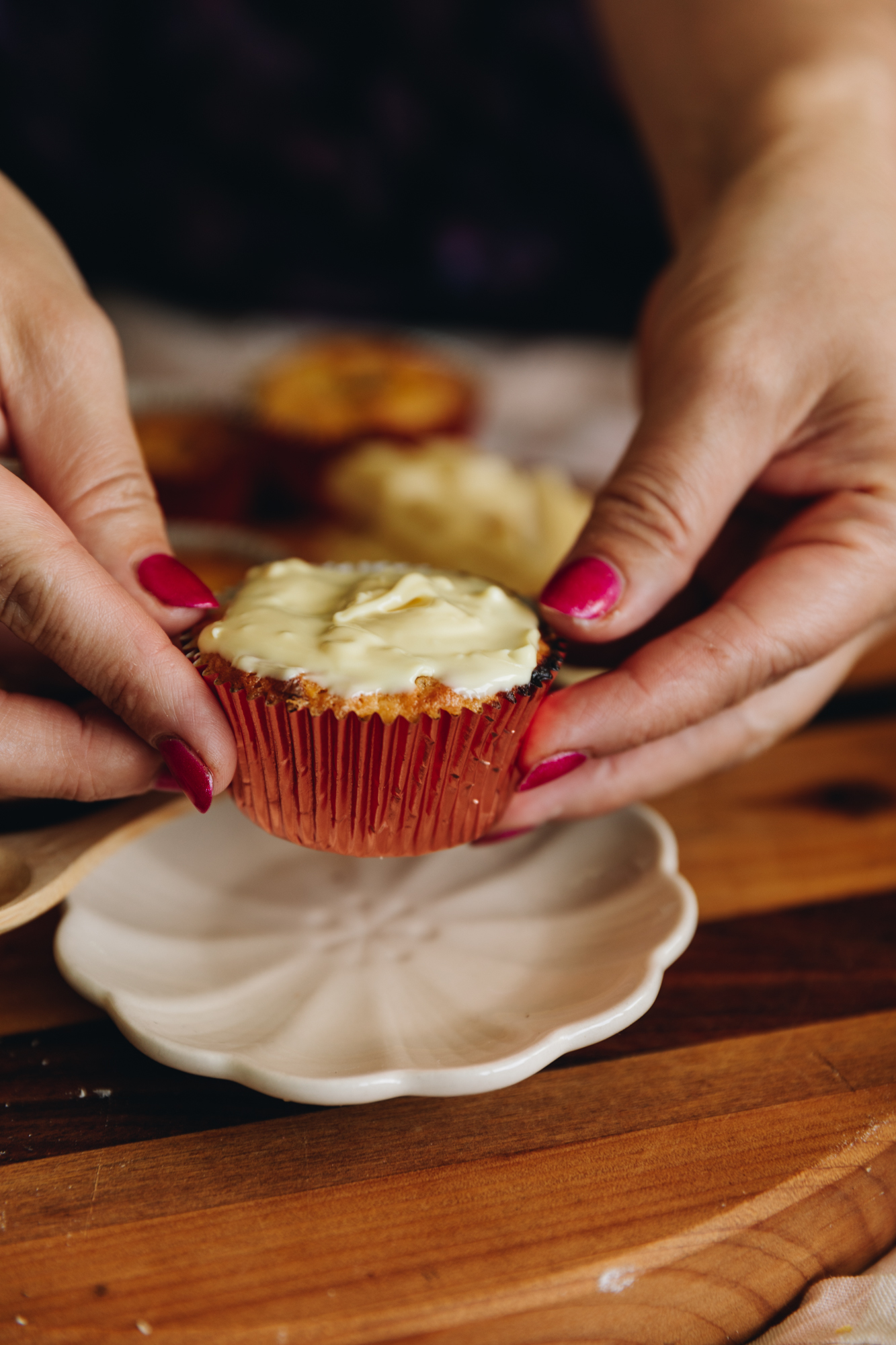 Naomi holds a passionfruit white chocolate muffins with melted white chocolate on it. It is hovering above a small white plate on a wooden board. 