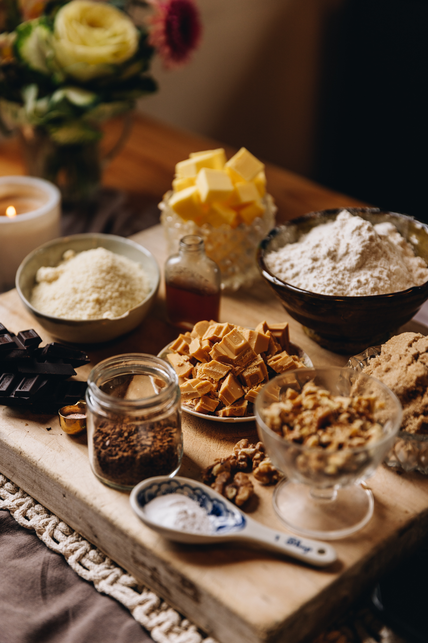 Ingredients in vintages bowls and spoons on a wooden board on a table cloth. Flowers in the background. 
