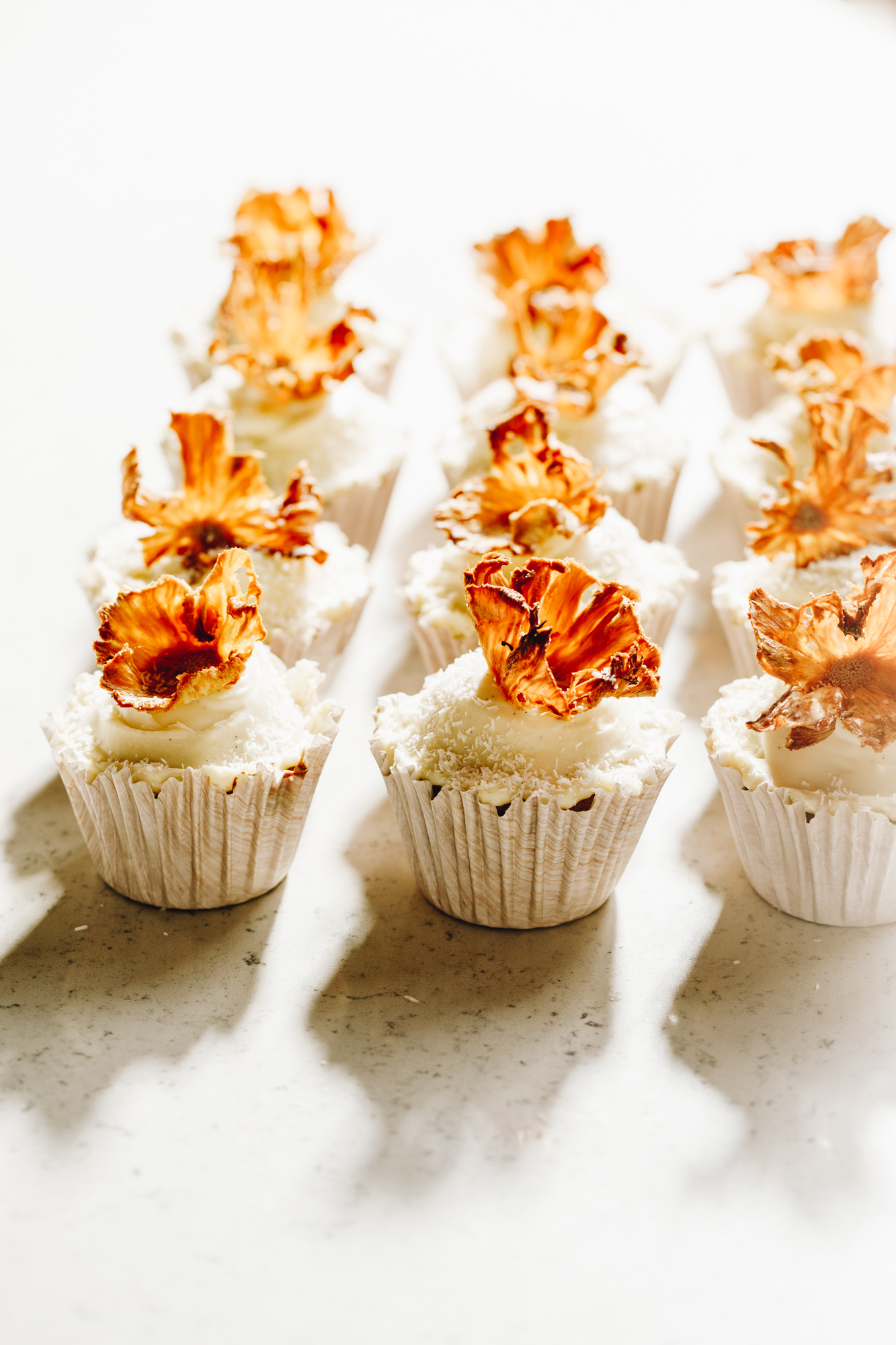 Cupcakes decorated with dried pineapple flowers on a white stone bench.