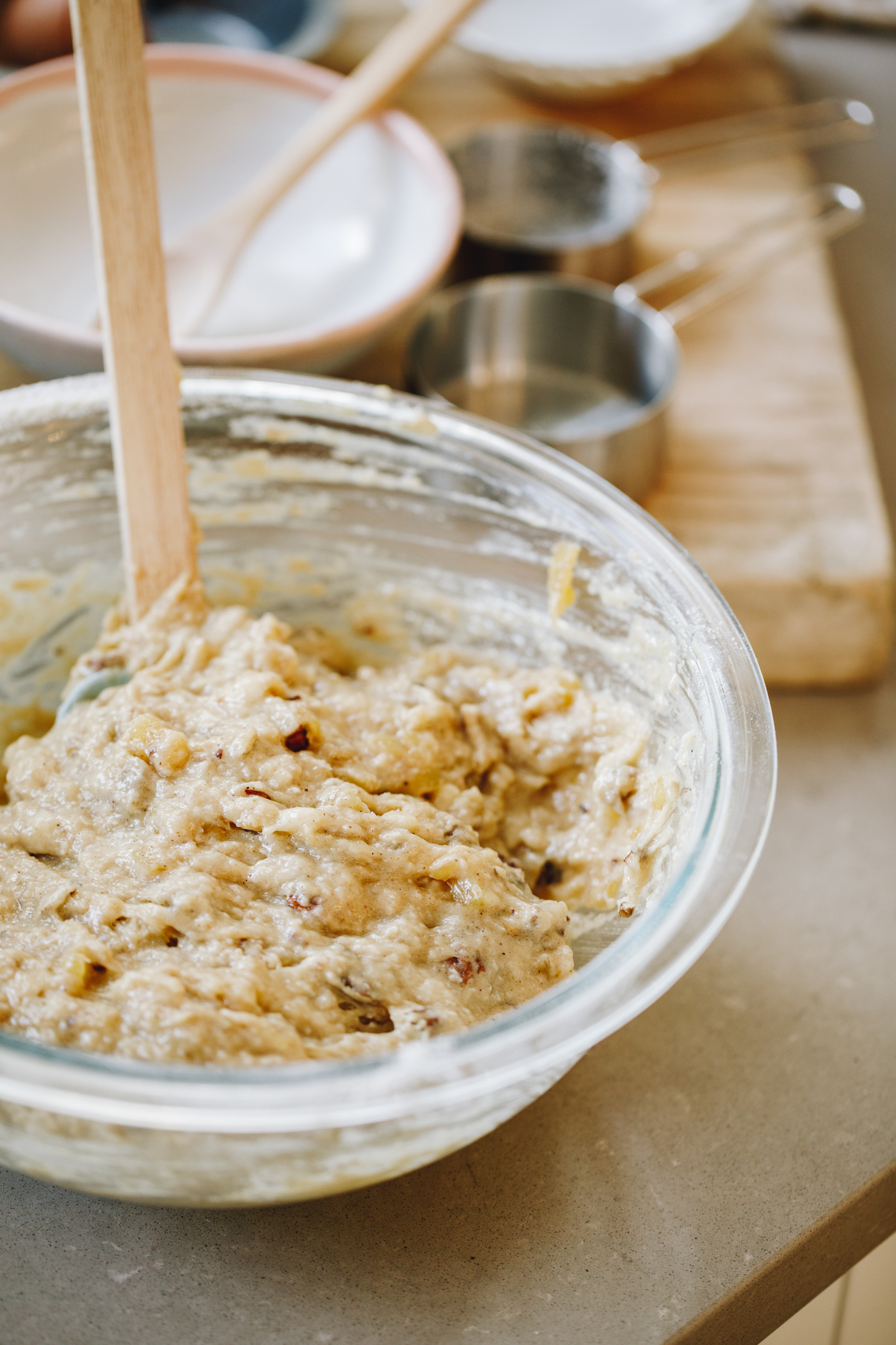 Banana and pineapple muffin mixture in a glass bowl with a spatula in it, on a stone bench.