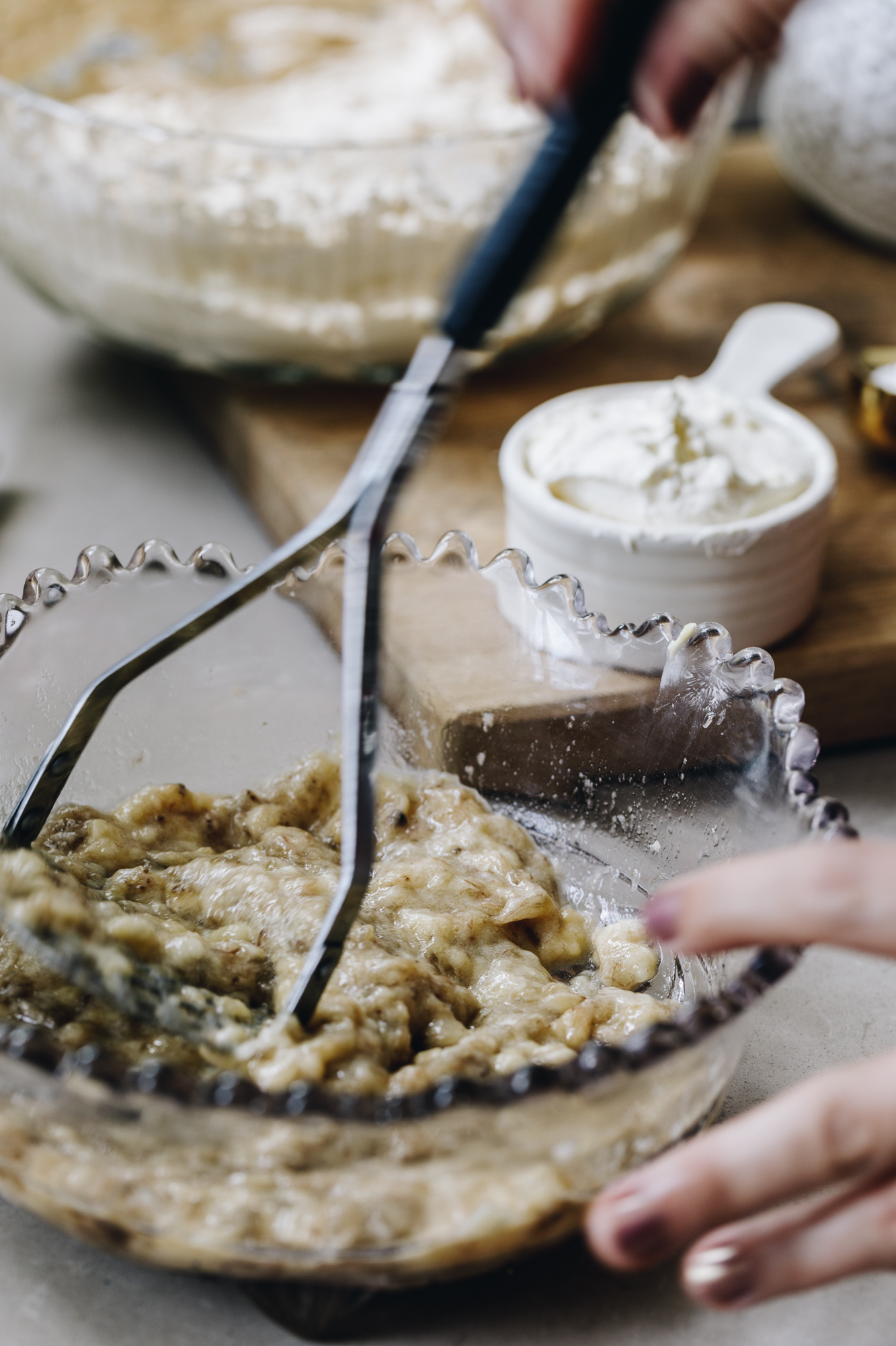 A vintage glass bowl with bananas mashed with a potato masher.