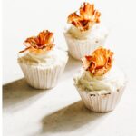 Three decorated hummingbird muffins, topped with cream cheese frosting and dried pineapple flowers.