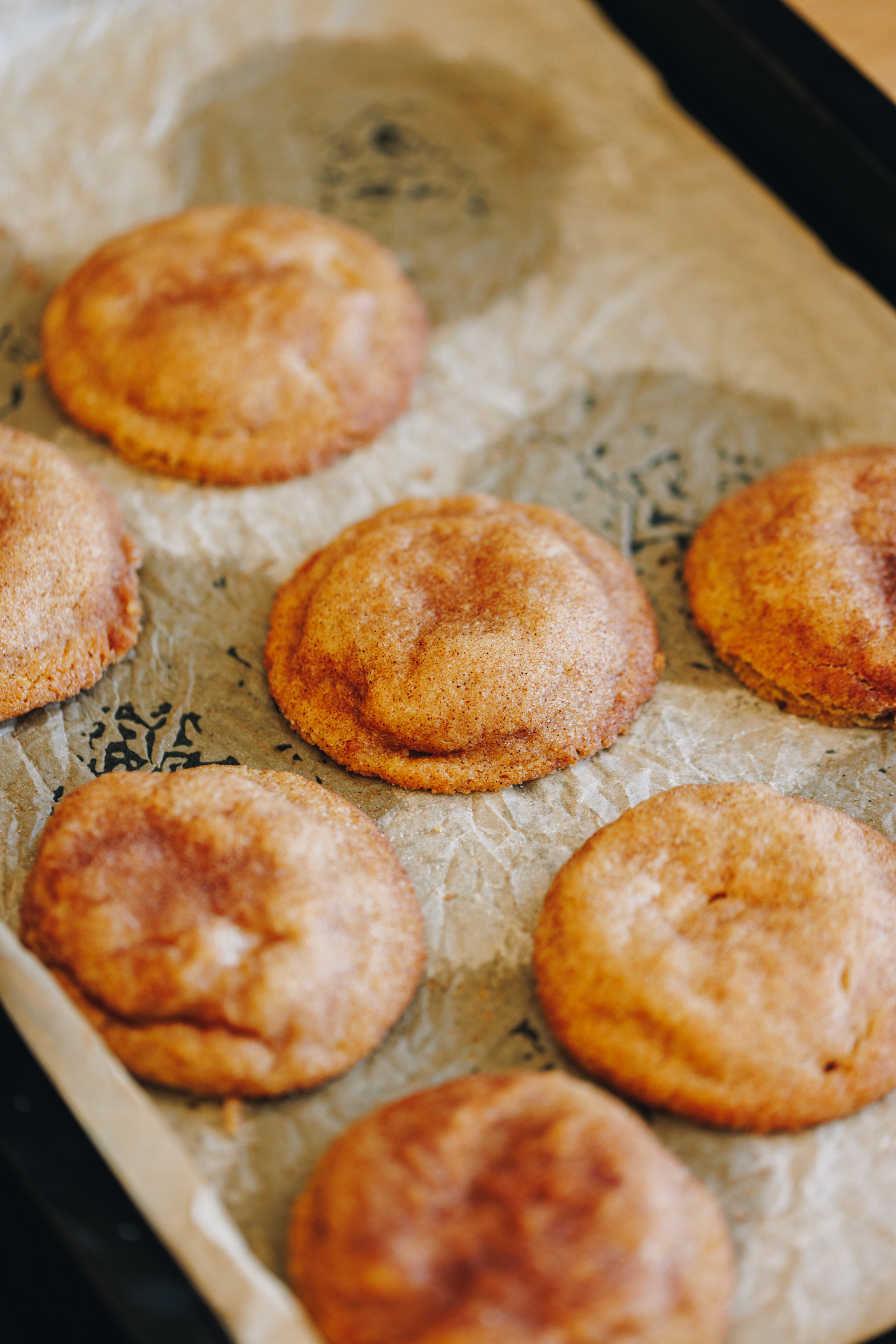 Baked peanut butter cookies on a tray with baking paper, sprinkled with cinnamon sugar. 