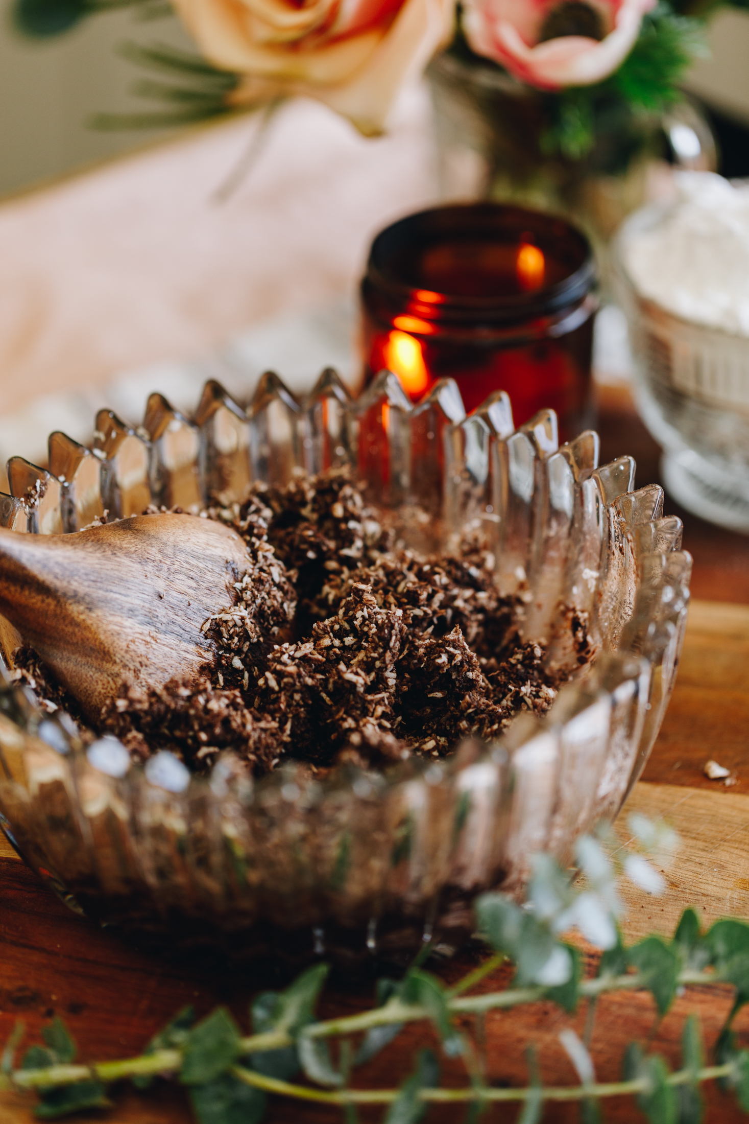 A coconut and cocoa mixture in a glass vintage bowl on a wooden table with a candle in the background.