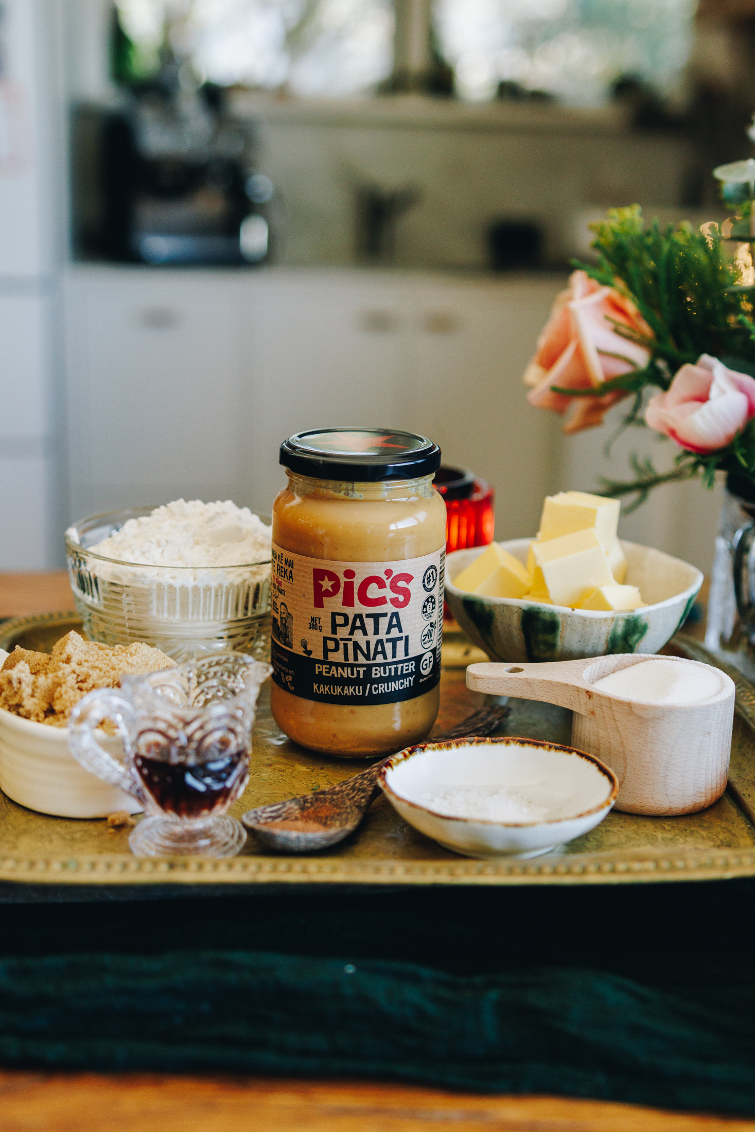 Ingredients for cookies on a wooden board in vintage bowls with flowers in the back. 